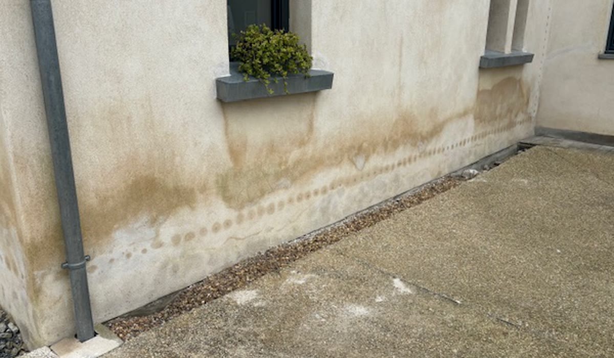 Façade extérieure portant des traces basses près d’une descente d’eau, de fenêtres et d’un sol minéral